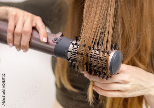 beautiful young woman using rotative brush hair styler for hair.female girl with long dark blonde hair.smiling woman in mirror. photo