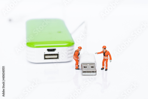 Miniature worker with USB cable and power bank isolate on white background, energy storage, technology industry 
