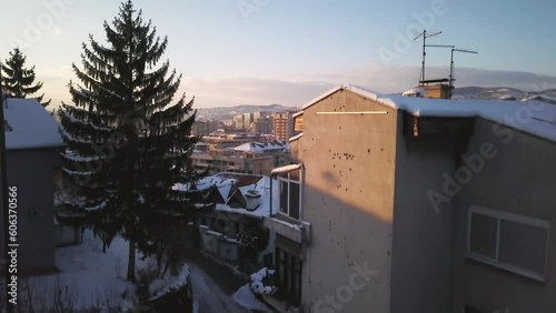 Aerial cinematic drone winter war zone bullet holes on building car driving Olympic downtown snowy frozen Sarajevo City town center Bosnia and Herzegovina frozen landscape sunset slow upward movement photo