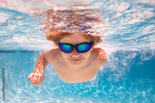 Kid swimming underwater. Summer kids. Happy little boy in swimming pool on summer day. Funny kid swimming and diving in pool. Kid underwater with splashes. Summer children water sports activity.