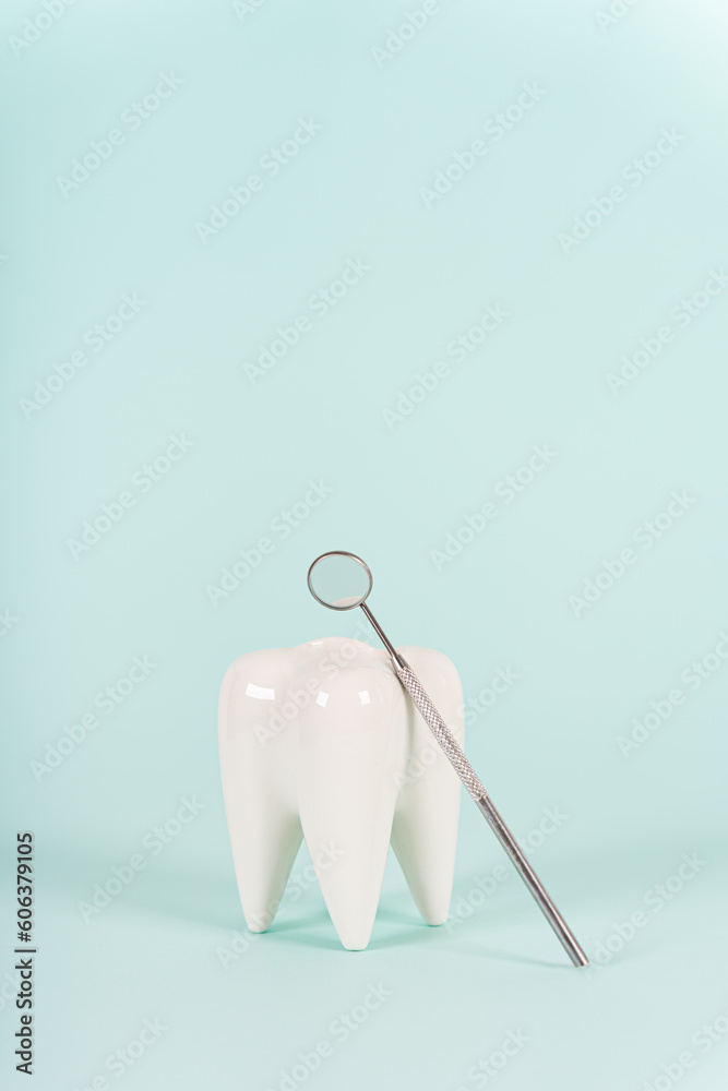 Healthy white tooth model and dentist mirror on blue background. Copy space. Teeth care, whitening, dental treatment, tooth extraction, implant concept. Dental clinic special offer. Vertical Healthy white tooth model and dentist mirror on blue background. Copy space. Teeth care, whitening, dental treatment, tooth extraction, implant concept. Dental clinic special offer. Vertical