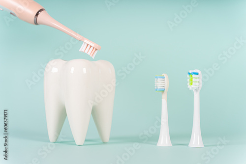 White healthy tooth model and a modern electric ultrasonic toothbrush with different toothbrush heads on blue background with copy space. Dental care and healthcare concept.