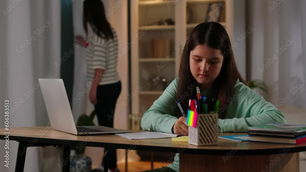 The girl uses the Internet on a laptop to do her homework. a brunette girl sitting at a table writes in a notebook and periodically looks at the laptop screen. The girl uses the Internet on a laptop to do her homework. a brunette girl sitting at a table writes in a notebook and periodically looks at the laptop screen.