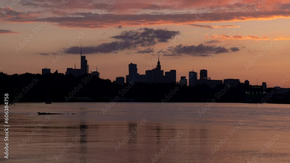 A time-lapse silhouette of skyscrapers across the river showing the dramatic formation of clouds and the transition from sunset to the darkness and lights of the city at night