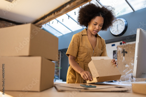 Female entrepreneur packing orders into cardboard boxes to ship photo