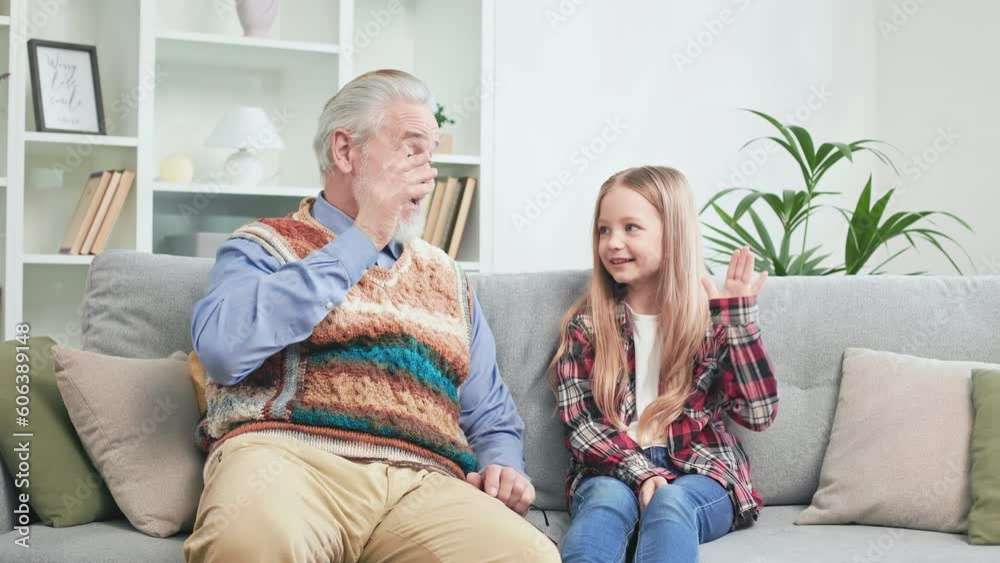 Pretty little kid enjoying day off at home and spending great time with loving grandfather. Emotional grandpa with granddaughter playing together and giving high five to each other. Pretty little kid enjoying day off at home and spending great time with loving grandfather. Emotional grandpa with granddaughter playing together and giving high five to each other.