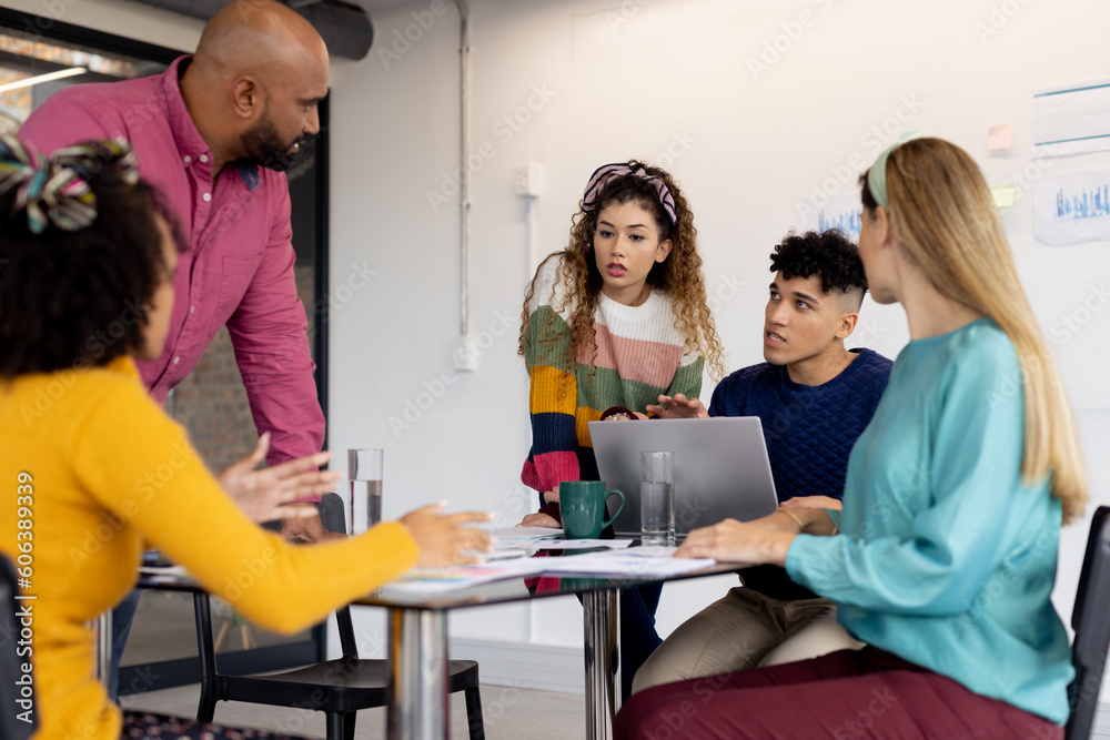 Busy diverse fashion designers using laptop and discussing work at meeting in office, unaltered Busy diverse fashion designers using laptop and discussing work at meeting in office, unaltered