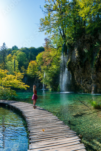 Woman traveler walking on wooden path trail with lakes and waterfall landscape in Plitvice Lakes National Park, UNESCO natural world heritage and famous travel destination of Croatia.