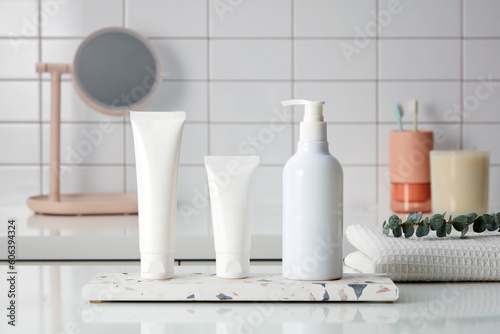 Some empty bottle container cream  cleanser or lotion displayed on a marble podium on tile wall background with toiletries  mirror and scented candles. Mockup for design. Advertising cosmetics.