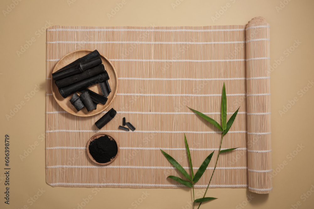 Minimal style, advertising photo for cosmetics product from bamboo charcoal extract. Top view of bamboo charcoal on wooden plate and green leaves decorated on brown bamboo mat