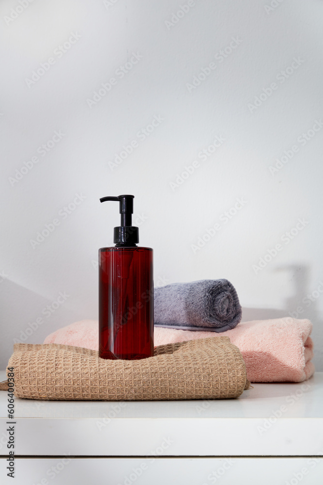 Minimal scene of an unbranded transparent pump bottle dispenser standing on a towel, decorated with other folded towels. Gentle skin care concept Minimal scene of an unbranded transparent pump bottle dispenser standing on a towel, decorated with other folded towels. Gentle skin care concept