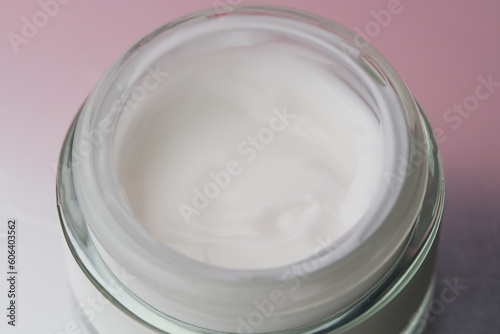 Glass jar with white face cream moisturiser on pink background.