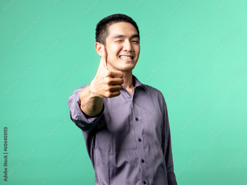 A portrait of an Asian man wearing a purple shirt, while making pointing with her thumb, isolated on a green background. A portrait of an Asian man wearing a purple shirt, while making pointing with her thumb, isolated on a green background.
