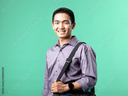 A portrait of an Asian man wearing a purple shirt, carrying a business bag, isolated on a green background.