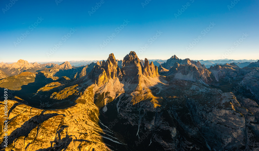 Majestic silhouette of Tre Cime di Lavaredo at sunrise. Spacious mountain landscape with rocky peaks and snow-covered slopes aerial view in back lit