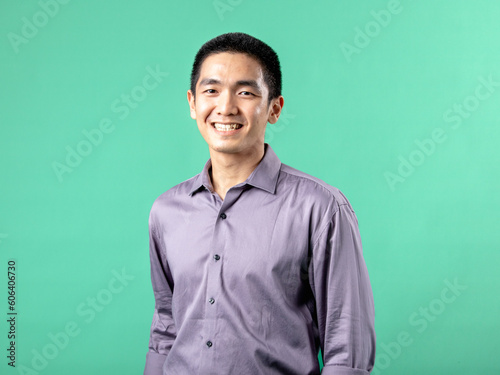 A portrait of an Asian man wearing a purple shirt, standing in a confident pose, isolated on a green background.