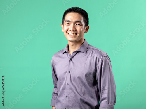 A portrait of an Asian man wearing a purple shirt, standing in a confident pose, isolated on a green background.