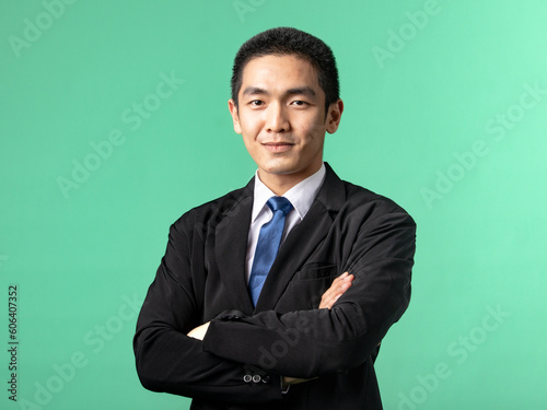 A portrait of an Asian man wearing a white shirt and a black suit, while folding his hands, isolated on a green background.