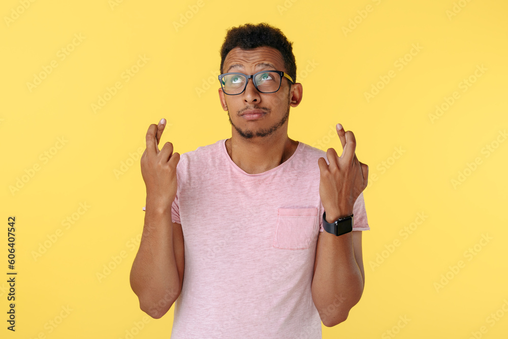 Hopeful african american young man holding fingers crossed in hope over yellow background. Hopeful african american young man holding fingers crossed in hope over yellow background.