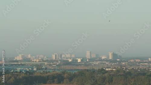 Orlando Florida skyline on a hazy morning. A helicopter enters the frame, a park can be seen in the foreground and hotels and buildings in the background. photo