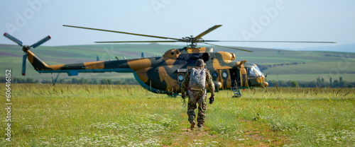 A soldier in camouflage goes to a military helicopter. Military helicopter with soldiers. Armed conflict, hostilities. Air armament, parachutist.