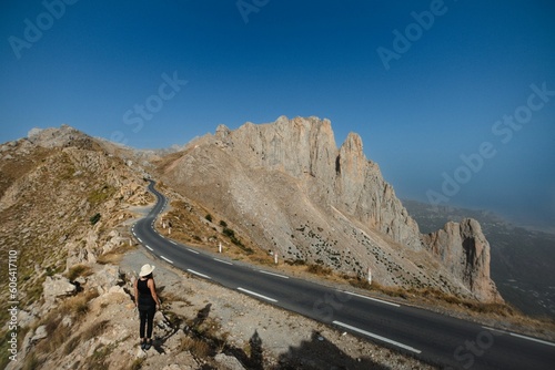Explorer person standing near a curving highway across the mountains