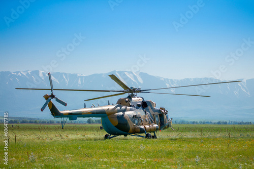 A military helicopter stands on the ground in a field with its propellers on. Armed conflict. Defense Army. Military aircraft on mission.