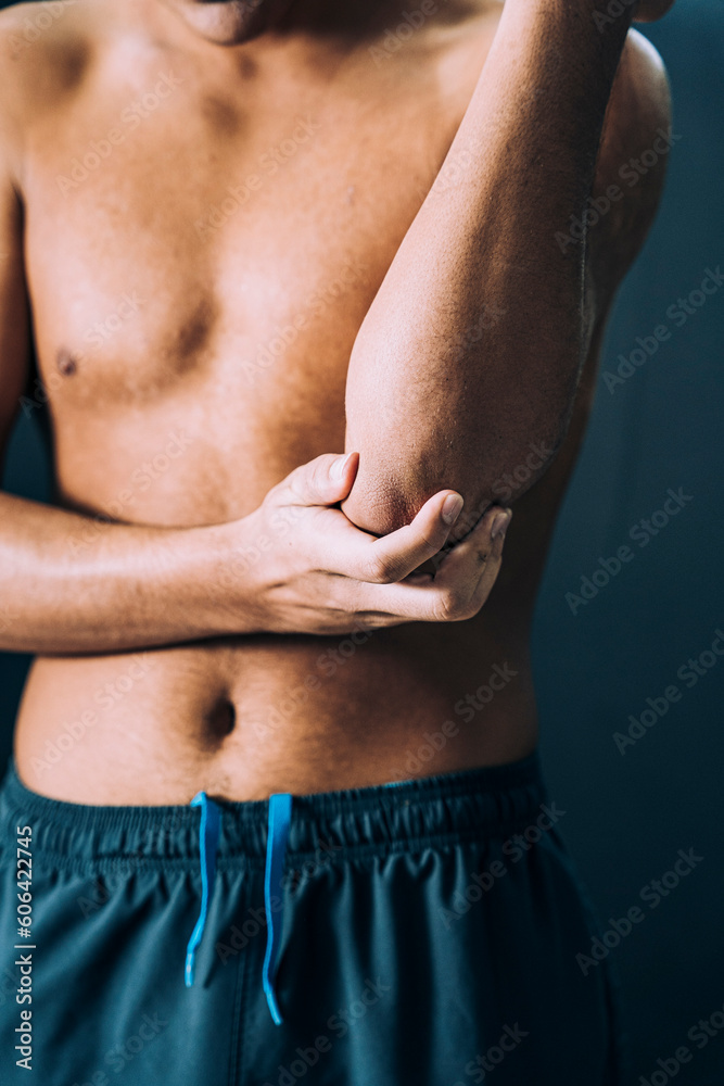 Vertical closeup of a shirtless Caucasian male athlete rubbing his right elbow in pain