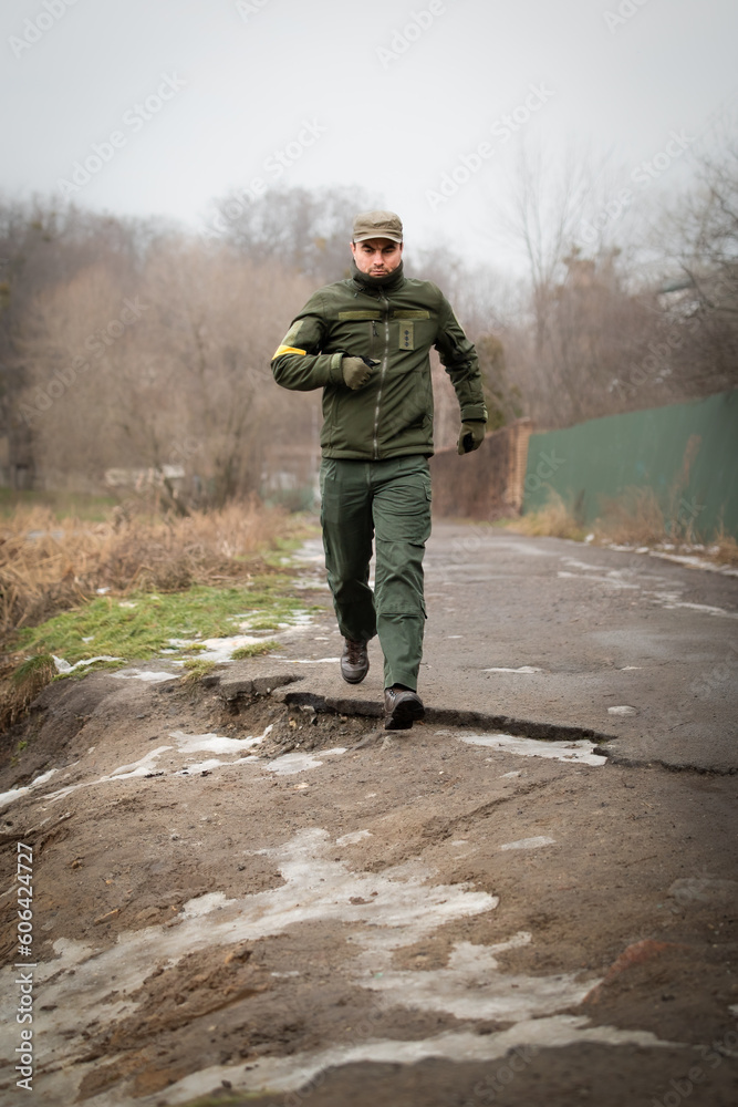 Serious military man in olive uniform and cap running forward in rural area on cold winter day
