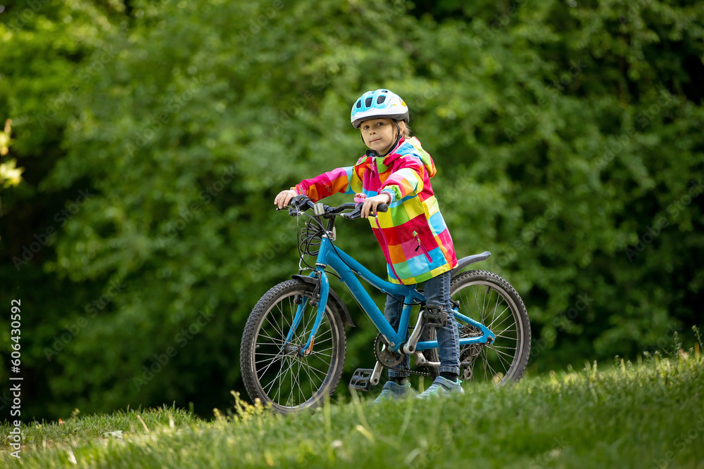 Fototapeta premium Happy kid boy, having fun in park with a bicycle on beautiful day. Active child wearing bike helmet