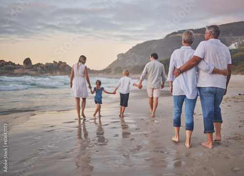 Family, generations and back with walking, beach and sunset with men, women and children with love. Parents, grandparents and kids by ocean, holding hands and bond on summer vacation with solidarity photo