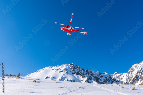 Red rescue helicopter moving in blue sky with blur propeller in winter mountains. Europe slovakia poland