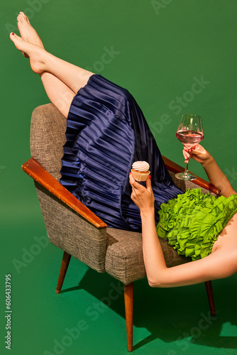 Sticker Woman lying on armchair, drinking rose wine and eating sweet muffin again green background