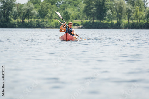 couple of sportive multiethnic friends in life vests sailing in kayak with paddles while spending summer weekend on river on blurred foreground, water recreation