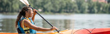 side view of active and happy african american woman in life vest holding paddle and sailing in kayak while spending summer weekend on scenic river, banner