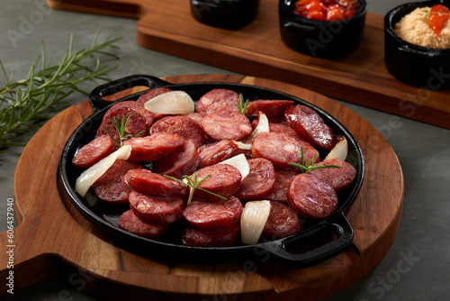 Portion of pepperoni sausage cut into slices. Served on a wooden board with a rustic iron plate.