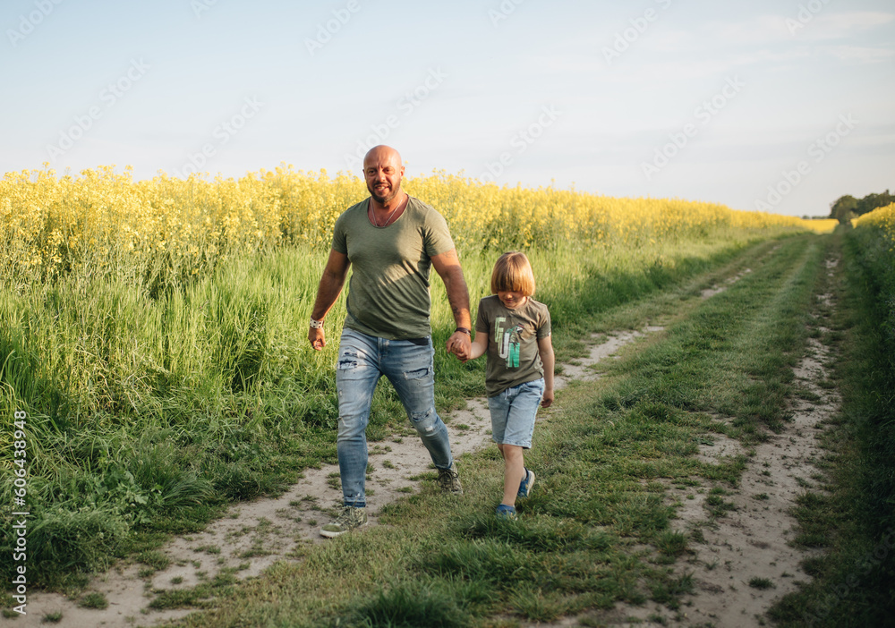 A man and a boy are walking and playing in a rapeseed field