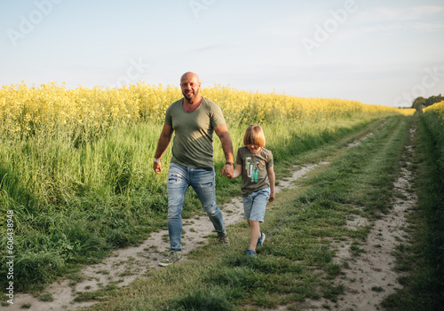 A man and a boy are walking and playing in a rapeseed field