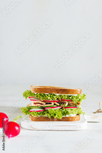 Delicious and fresh sandwich with greens, ham, cucumber and radish on a wooden board on a light background in the foreground with radish