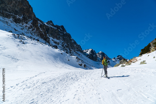 view of active woman ski touring at mountains background at sunny winter day. Ski mountaineer with red jacket walking up along a steep snowy ridge with the skis in the backpack