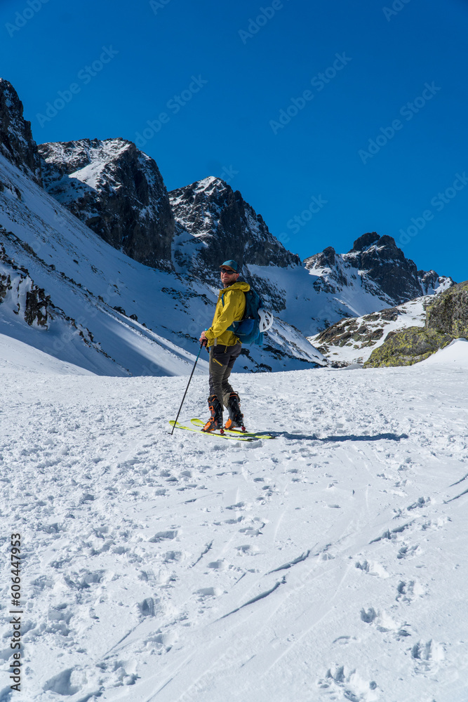 view of active man ski touring at mountains background at sunny winter day. Ski mountaineer with red jacket walking up along a steep snowy ridge with the skis in the backpack