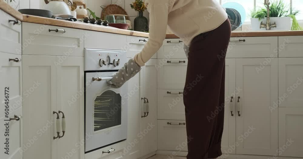 Pregnant Caucasian woman standing in the kitchen, preparing a delicious meal. With confidence, she takes a tray of prepared food and carefully places it in the oven, using oven mitts to protect. Pregnant Caucasian woman standing in the kitchen, preparing a delicious meal. With confidence, she takes a tray of prepared food and carefully places it in the oven, using oven mitts to protect.