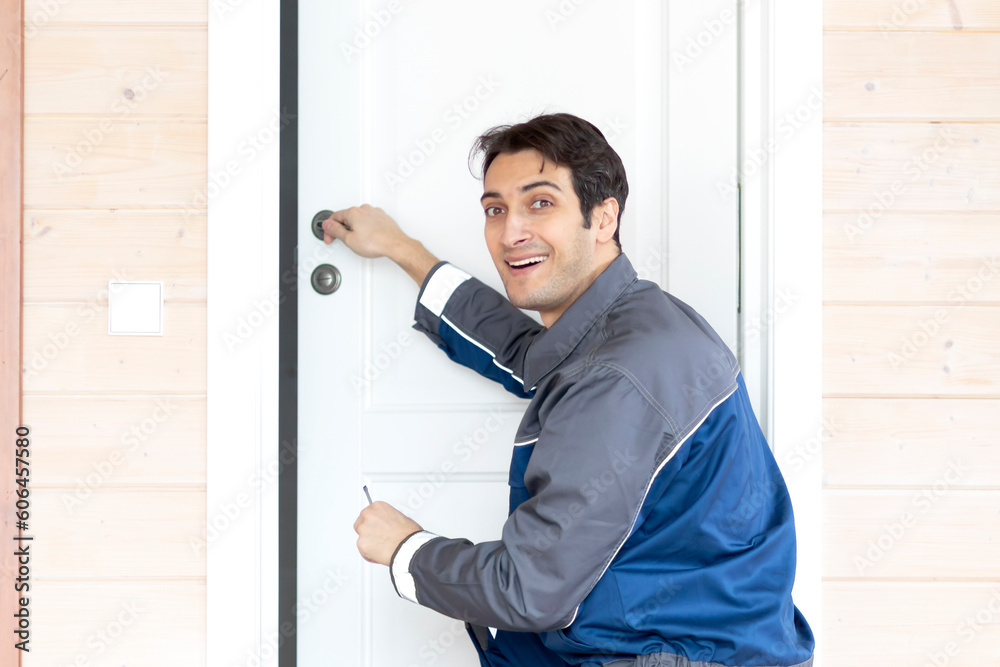 Fototapeta premium Installation of a wooden door. Portrait of young smiling handyman in blue uniform installing door. Professional repair service and maintenance concept