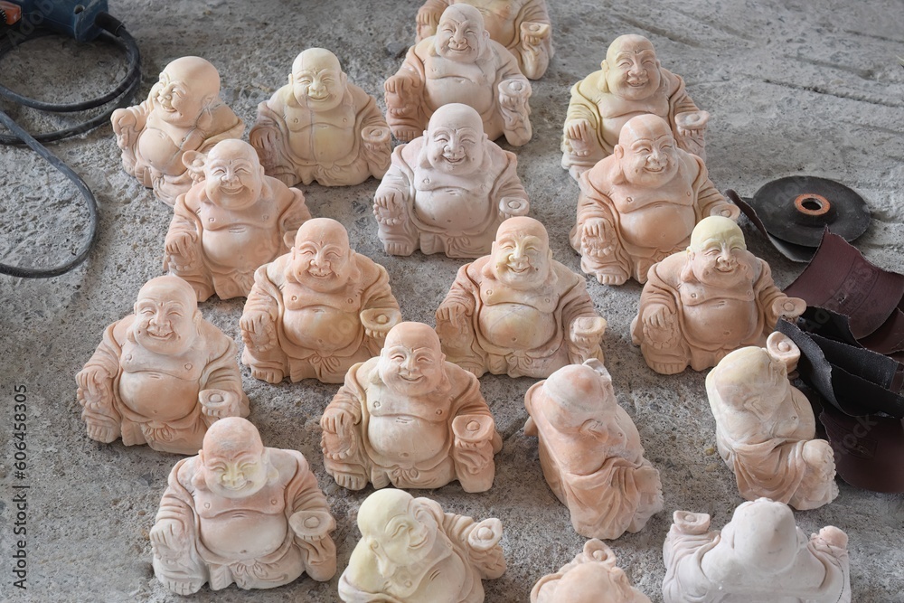 Collection of Laughing Buddha statuettes being polished near Ha Long Bay, Vietnam - obrazy, fototapety, plakaty 