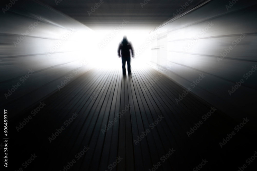 Blurred background with a silhouette of a man in a dark tunnel and light at the end