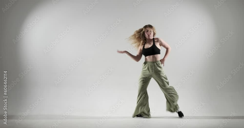 Curly-haired Caucasian dancer on white background as she unleashes her jazz funk skills, with dynamic movements and infectious energy. She wearing green pants and black top. Curly-haired Caucasian dancer on white background as she unleashes her jazz funk skills, with dynamic movements and infectious energy. She wearing green pants and black top.