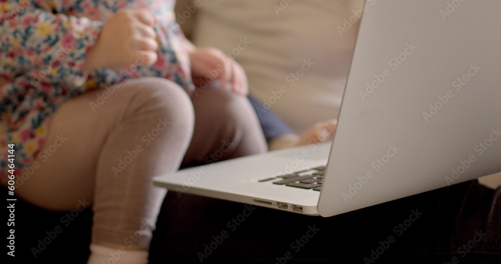 Naklejka premium The Child hand opens the laptop, readiness to view the monitor. Parents are sitting nearby, assisting the girl. Use gadget natural light.