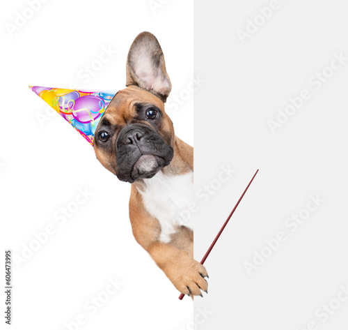 French bulldog puppy wearing party cap points away on empty space. isolated on white background © Ermolaev Alexandr