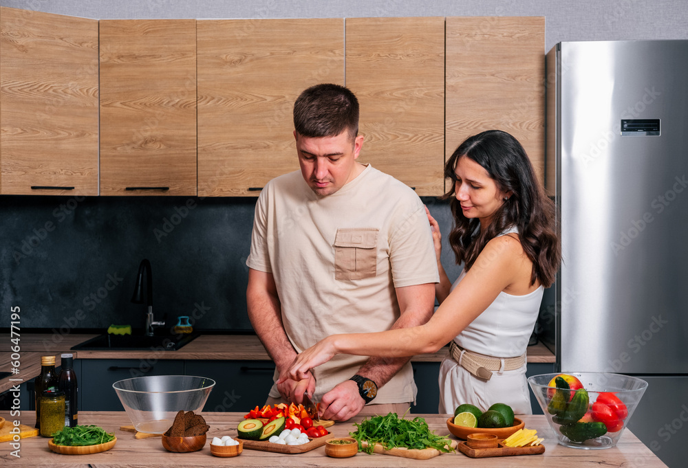 A young couple is preparing a salad. The wife tells her husband what to cook in the kitchen.