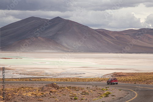 A red car on road at Piedras rojas in Atacama desert, colorful landscapes of a Salt Flat and the altiplano lakes with black volcanos at the background, situated in the heart of the Chilean altiplano